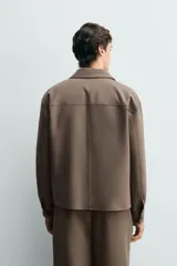 Sobrecamisa negra de corte boxy fit en tejido compacto, con cuello solapa, manga larga con puño abotonado, bolsillos frontales aplicados y cierre frontal de botonadura.