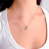 Collar de cadena fina dorada con un dije circular que combina un borde metálico dorado, un centro de nácar y una pequeña sección superior decorada con cristales.