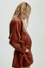 Falda mini de estilo globo confeccionada en material con efecto piel color marrón. Presenta diseño abullonado, bolsillos delanteros de plastrón y cierre frontal con cremallera y botón a presión.