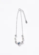 Pulsera de plata 925 con cadena de eslabones finos, decorada con pequeñas zirconias blancas engarzadas y un dije central en forma de corazón con una zirconia celeste rodeada de zirconias blancas.