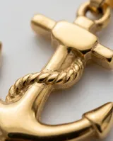 Dije de acero con baño de oro en forma de ancla con detalle de soga grabada.