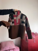 Buzo de diseño único confeccionado con una combinación de corderito marrón y paneles de tejido vintage con estampado geométrico en tonos gris, negro y bordó. Presenta cuello alto con cierre frontal y mangas largas.