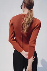 Chaqueta de punto color óxido, con cuello redondo, manga larga abullonada y cierre frontal con botones.