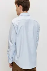 Camisa de manga larga con cierre frontal de botones y cuello clásico, color celeste con sutiles rayas verticales.