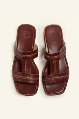 Sandalia plana de cuero color marrón, con tiras anchas y costuras blancas a la vista. Tiene punta cuadrada y un pequeño taco de 2 cm.