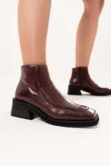 Bota corta de cuero color bordó, con punta cuadrada, taco bloque y plataforma. Presenta cierre lateral interno y detalle de ribete en la capellada.