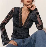 Top de encaje negro con diseño floral, escote en V profundo con terminación de puntilla, mangas largas acampanadas y ajuste al cuerpo.