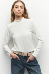 Polera blanca de tejido texturizado, cuello alto y mangas largas.