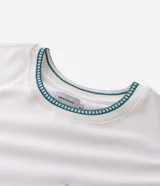 Remera de algodón marca Marfinno, color blanco, con cuello redondo y detalle de ribete en contraste. Presenta un diseño de cuatro sellos bordados en el pecho.