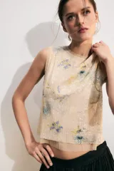 Top corto sin mangas, con cuello redondo, confeccionado en tejido de punto cubierto de lentejuelas con estampado floral en tonos azules y verdes sobre fondo beige. Cuenta con cierre en la espalda con abertura y botón.