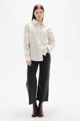Camisa de algodón con diseño de rayas verticales finas en tonos neutros, corte holgado, cuello camisero y cierre frontal con botones.