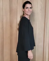 Remerón de textura acanalada en color gris claro, con cuello redondo, mangas largas y bolsillo frontal en el pecho. Presenta un diseño holgado con corte asimétrico, siendo más largo en la parte posterior.