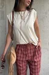Remera sin mangas de color manteca, con detalle de tachas metálicas doradas en los hombros.