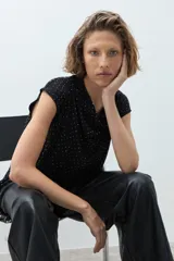 Blusa negra con pequeños puntos brillantes, cuello drapeado y mangas cortas.