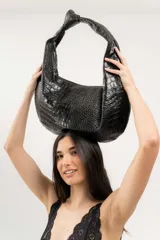 Bolso tipo hobo de cuero marrón con textura de piel de cocodrilo, asa anudada y cierre superior abierto.
