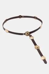 Cinturón de piel color marrón oscuro con aplicaciones metálicas doradas de estilo western o concho. Incluye una hebilla de gancho a presión y una tira colgante decorativa con múltiples apliques circulares con relieve de flor o sol.