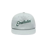 Gorra Eme Studios color gris claro con visera plana y bordado en relieve verde oscuro con borde blanco en el frente.
