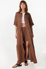 Vestido camisero largo de lino italiano color celeste, de corte relajado, con mangas caídas, jareta ajustable en la cintura, cierre frontal de botones y bajo con volado fruncido.