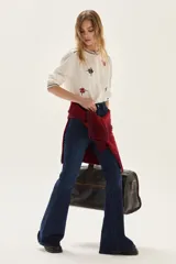 Camisa de algodón color crudo con cuello mao y cierre frontal de botones. Presenta bordados florales en tonos rojo y negro distribuidos en el cuerpo, cuello y puños.