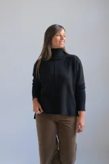Polerón negro de cuello alto, con diseño de costura vertical central y puños acanalados. Presenta un corte holgado con dobladillo asimétrico, siendo más largo en la parte posterior.