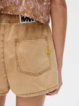 Short de denim color beige con cintura elástica y cordón ajustable. Presenta un bolsillo trasero con un pequeño bordado de sol en color amarillo.