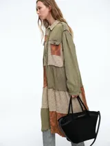 Vestido camisero de corte midi con diseño patchwork que combina paneles en tonos crudo y marrón con estampados florales sutiles. Presenta cierre frontal con botones, cuello camisero y mangas largas con puños.