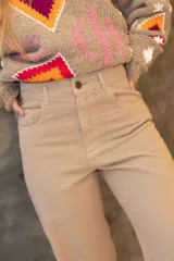 Pantalón vaquero de tiro alto y corte recto en color beige. Presenta tajos laterales en el bajo con detalles en cuero y terminación deshilachada. Incluye botón de guampa y detalle de pespuntes en los bolsillos traseros.
