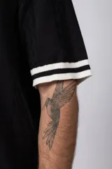 Camisa de punto de manga corta con cuello tipo bowling y cierre frontal de botones. Presenta un diseño texturizado con franjas verticales y detalles de contraste en blanco en los bordes de las mangas.