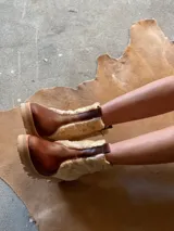 Botas de cuero marrón con la caña recubierta de corderito verde. Presentan una suela de plataforma tipo track en color beige y un tirador en la parte posterior para facilitar el calce.