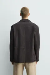 Blazer de corte relajado confeccionada en piel con acabado de ante. Presenta cuello con solapas de muesca, cierre frontal de dos botones, mangas largas y bolsillos de plastrón en la parte delantera. Destaca por sus costuras con efecto lavado que le otorgan un aspecto vintage.