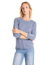 Buzo de tejido fino en color azul grisáceo, con cuello redondo y mangas raglán tres cuartos. Presenta una línea de tachas decorativas a lo largo de la parte superior de las mangas.