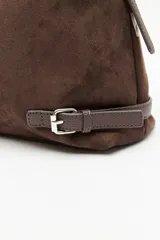 Cartera de gamuza negra con textura suave y acabado aterciopelado. Cuenta con una silueta amplia y flexible, cierre superior metálico, correa regulable y detalles laterales con hebillas.