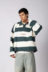 Buzo tipo polo de corte boxy, con diseño de franjas horizontales anchas en color verde oscuro y crema. Presenta cuello camisero, cierre frontal parcial y detalles de costuras desflecadas. Incluye logo bordado en el pecho.