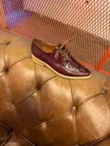 Zapato acordonado de cuero color burdeos, con detalle de trenzado en la parte delantera y suela de goma color crema.