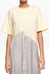 Vestido midi de línea A con diseño bimateria. Parte superior de tejido de algodón color amarillo claro con escote redondo y mangas cortas, y parte inferior de tejido satinado gris con caída fluida. Cuenta con detalle de encaje superpuesto en la unión con acabado irregular.