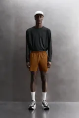 Pantalón corto deportivo color marrón oliva, confeccionado en tejido técnico ligero y elástico, con forro interior. Presenta cintura elástica ajustable con cordón, bolsillos frontales, bolsillo de seguridad trasero con cierre y aberturas laterales en el bajo.