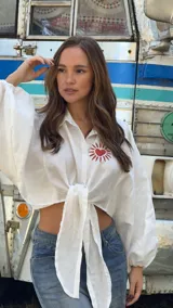 Camisa de lino blanca con mangas largas abullonadas y nudo frontal. Presenta un bordado artesanal en el pecho con diseño de sol y corazón en color rojo.