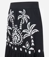 Pollera midi de algodón con diseño acampanado y cierre lateral. Presenta un estampado contrastante de palmeras y motivos arabescos sobre fondo oscuro.