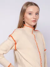 Polera de punto color beige con cuello alto, manga larga y detalles de costura overlock en color naranja.