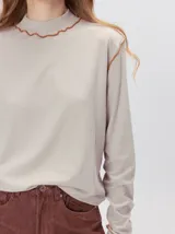 Polera de manga larga confeccionada en tela rib color bordó, con cuello alto y hombreras. Presenta costuras a la vista con pespuntes en hilo de color contrastante en el cuello, puños, hombros y ruedo.