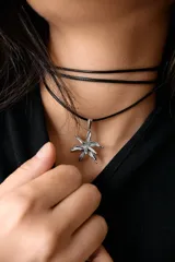 Collar con dije de acero quirúrgico en forma de flor de lirio, montado sobre un tiento de cuero encerado largo.