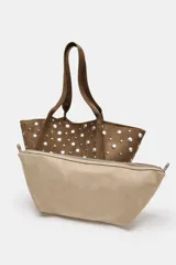 Bolso tipo shopper de hombro, confeccionado en gamuza color marrón, decorado con tachas metálicas plateadas en toda su superficie. Cuenta con doble asa de hombro y cierre mediante botón imantado.