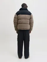 Campera puffer con diseño de bloques de color, combinando tejido teddy en tono arena y paneles negros en los hombros. Presenta cuello alto, cierre frontal y diseño acolchado.