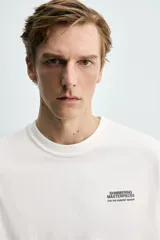 Camiseta de corte relajado, cuello redondo y manga corta. Presenta un pequeño estampado de texto en el pecho y un estampado gráfico de mayor tamaño en la espalda.