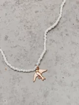 Collar corto de cuentas blancas con dije de golondrina dorada.