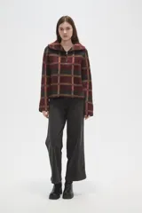 Sweater de tejido jacquard con diseño a cuadros en tonos bordó, negro y beige. Presenta un corte holgado, cuello solapa amplio y cierre frontal parcial con cremallera.