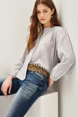 Camisa de algodón color celeste claro, con textura sutil y pequeños bordados blancos en forma de rombos. Presenta cuello mao, botones frontales y mangas largas abullonadas con puños ajustados.