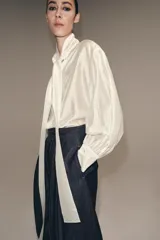 Camisa de corte holgado confeccionada en tejido satinado con mezcla de lyocell. Presenta cuello redondo con escote en pico y lazada frontal integrada. Cuenta con mangas largas abullonadas terminadas en puños anchos y bajo recto.