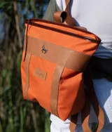 Mochila de lona color naranja con detalles y tiras regulables de cuero marrón, marca Sierra Mora, con aplique metálico de caballo.