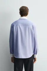 Camisa de corte regular fit confeccionada en tejido ligero de algodón, con diseño de rayas verticales azules y blancas. Presenta cuello abotonado y puños en color blanco a contraste, con cierre frontal de botones.